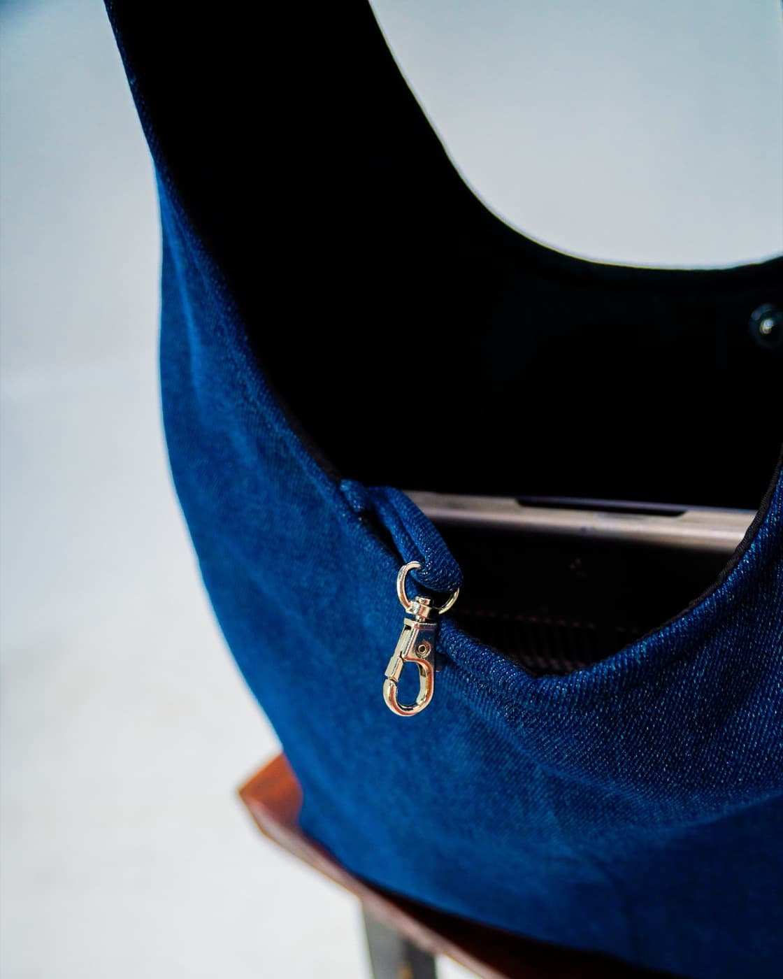 Crescent-shaped indigo denim hobo bag with a brass snap hook