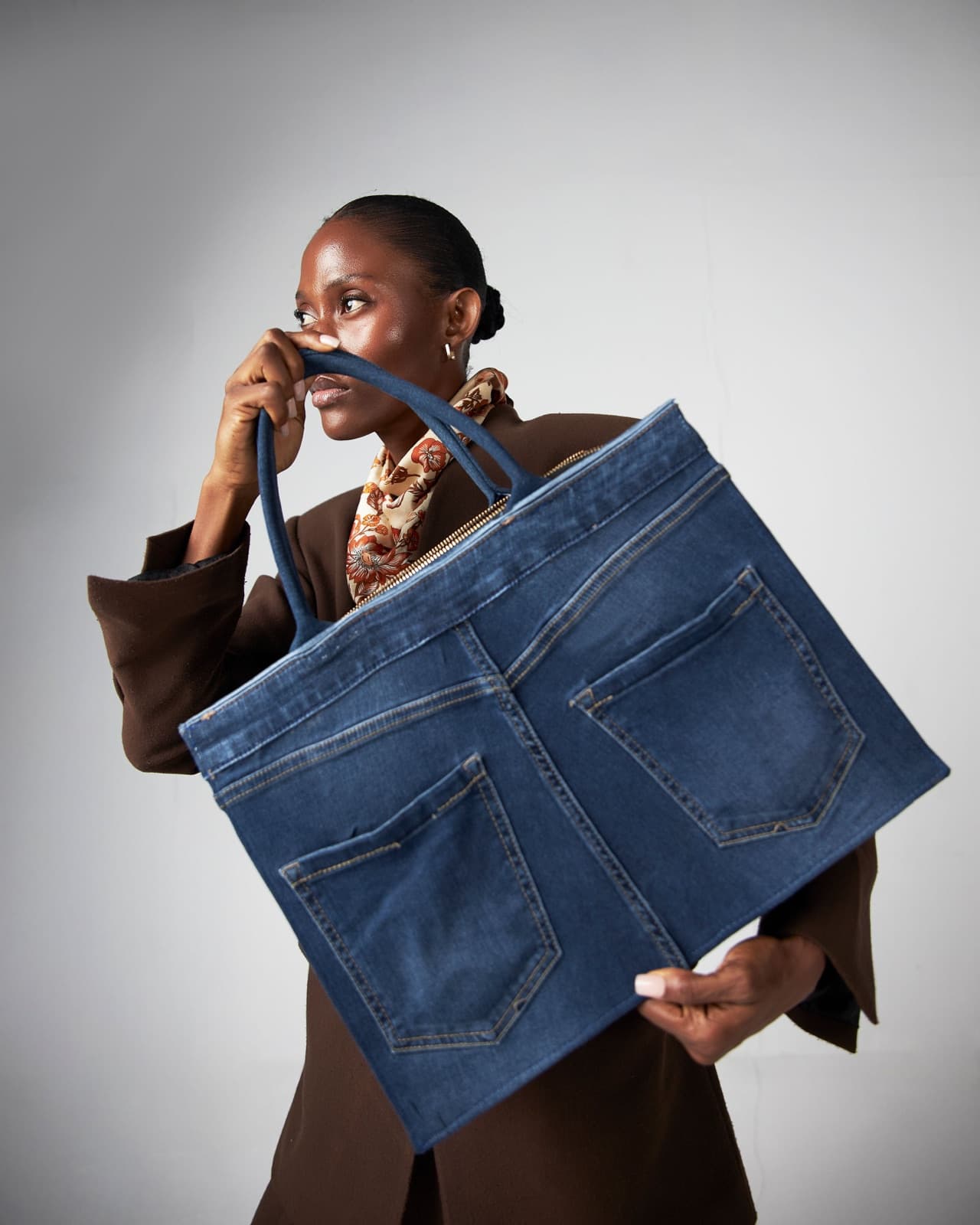 Model in a brown coat holding a large upcycled denim tote made from jean panels